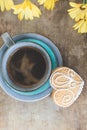 Top view of yellow flowers, blue cup of coffee and a gingerbread cookie on old wooden rustic background Royalty Free Stock Photo