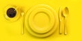 Top view of yellow plate, fork, knife, spoon and cup of coffee on yellow grunge table