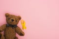 Top view of yellow ribbon near teddy bear on pink background, international childhood cancer day concept.