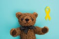 Top view of yellow ribbon next to teddy bear on blue background, international childhood cancer day concept.