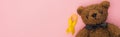 Top view of yellow ribbon and teddy bear on pink background, panoramic shot, international childhood cancer day concept.