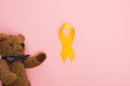 Top view of yellow ribbon and toy on pink background, international childhood cancer day concept.