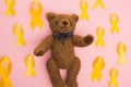 Top view of yellow ribbons around teddy bear on pink background, international childhood cancer day concept.