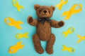 Top view of yellow ribbons and brown teddy bear with bow on blue background, international childhood cancer day concept.