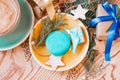 Top view on yellow saucer with blue macaron, with Christmas gift, wooden decorations and cup of cappuccino.