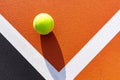 Top view of a yellow tennis ball on an orange court with white baselines