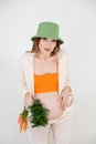 Young beautiful pregnant woman with long dark hair wear green bucket hat, sitting, holding belly and bunch of carrots. Royalty Free Stock Photo