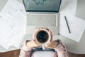 Top view. Young business woman sitting at table with cup of coffee and working on the laptop with graphics and charts