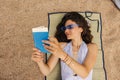 Top view young caucasian woman in blue sunglasses reading book on beach sand. Royalty Free Stock Photo