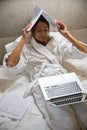 Young exhausted businesswoman with laptop covering her head with papers on bed