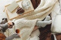 Top view of young girl covered with cozy white blanket siting on bed drinking tea and eating