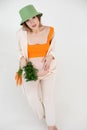 Young gorgeous pregnant woman with long dark hair wear green bucket hat, sitting, holding belly and bunch of carrots. Royalty Free Stock Photo