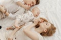 Top view of young happy idyllic family in white clothes with smiling plump blue-eyed baby infant lying on white bed.