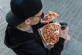 Top view on a young hipster man in black clothes in sunglasses in a cap with a piece of pizza with a glass bottle