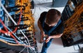 Top view of young man in uniform with measuring device that works with internet equipment and wires in server room Royalty Free Stock Photo