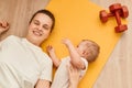 Top view of young mother with her baby daughter lying on the fitness mat during the exercise with dumbbells on the floor, resting Royalty Free Stock Photo