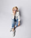 Top view of young positive blonde woman in casual clothing, white sneakers and sunglasses sitting on floor and smiling Royalty Free Stock Photo