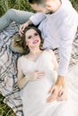 Top view of young smiling pregnant woman in white dress, lying on legs of her bearded man, enjoying the rest on the Royalty Free Stock Photo