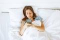 Top view young woman awaken in white cozy bed using smartphone gadget, millennial female wake up lying in bed against Royalty Free Stock Photo