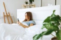 Top view young woman awaken in white cozy bed using smartphone gadget, millennial female wake up lying in bed against Royalty Free Stock Photo