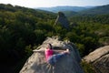 Top view of young woman doing yoga exercises lying on top of big mountain rock on bright summer day