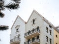 Top of a white building with a double triangular roof against the sky during a snowfall