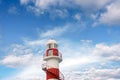 Top of a white-red lighthouse against a blue sky with an airplane Royalty Free Stock Photo