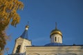 White wall of the Orthodox Church with arched relief, bell tower, blue roofs and gilded domes of crosses, birch crown on the left