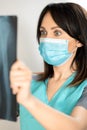 The topic of coronavirus and safety. A young female surgeon with dark hair in a mask from a virus looks at an X-ray in surprise. Royalty Free Stock Photo