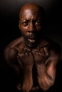 Topless black man in shadows with hands clenched.