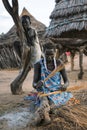 TOPOSA TRIBE, SOUTH SUDAN - MARCH 12, 2020: Woman sitting on dirty ground near hut and kid and weaving product from straw in