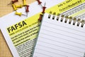 Topview photo of FAFSA - free application for federal student aid, and open notepad with blank space