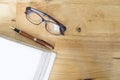 topview of wooden working desktop in office. Glasses, pen and empty white book page.