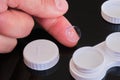 Toric contact lens on fingertip with white contact lens case and cap - composition on black reflective background