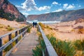 Torists walking to Cala Domestica beach on wooden pier. Windy summer scene of Sardinia, Italy, Europe.