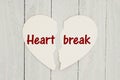 Torn heart-shape card on weathered wood background with text Heartbreak