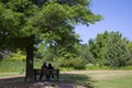 Couple sitting on a park bench under a tree. Relaxing in a public park in the morning Royalty Free Stock Photo