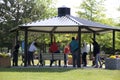 Group of people doing outdoor stretch exercise under a pavilion on a hot summer day