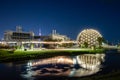 The Cinesphere Theatre globe lit up and reflecting in water at Ontario Place Marina with the CN Tower in the distance.