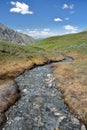 A torrent near Refuge Agnel near Agnel pass, with mountains covered with snow in the background Royalty Free Stock Photo