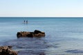 Landscape of coast and two athletes practicing paddle surfing in the distance