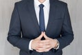 Torso of anonymous businessman standing with hands in lowered steeple, wearing beautiful fashionable classic navy blue