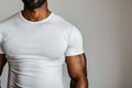 Torso portrait of a black well-built man stands against a neutral grey backdrop, showcasing his upper body physique. His muscular