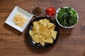 Tortilla chips on a black crockery with various vegetables and minced meat on a wooden table. Royalty Free Stock Photo