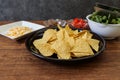 Tortilla chips on a black crockery with various vegetables and minced meat on a wooden table. Royalty Free Stock Photo