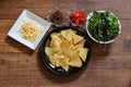 Tortilla chips on a black crockery with various vegetables and minced meat on a wooden table Royalty Free Stock Photo