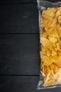 Tortilla Mexican nachos  chips in a plastic  bag, on black wooden background, top view or flat lay with copy space for text Royalty Free Stock Photo