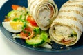 Tortilla wrap with chicken and beechwood smoked bacon served with mix salad on the blue plate