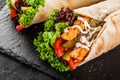 Tortilla wraps with grilled chicken fillet, fresh vegetables and salad on black stone background. Healthy snack or take-away lunch