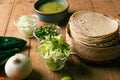 Tortillas, bowl with green sauce and vegetables on a wooden table.